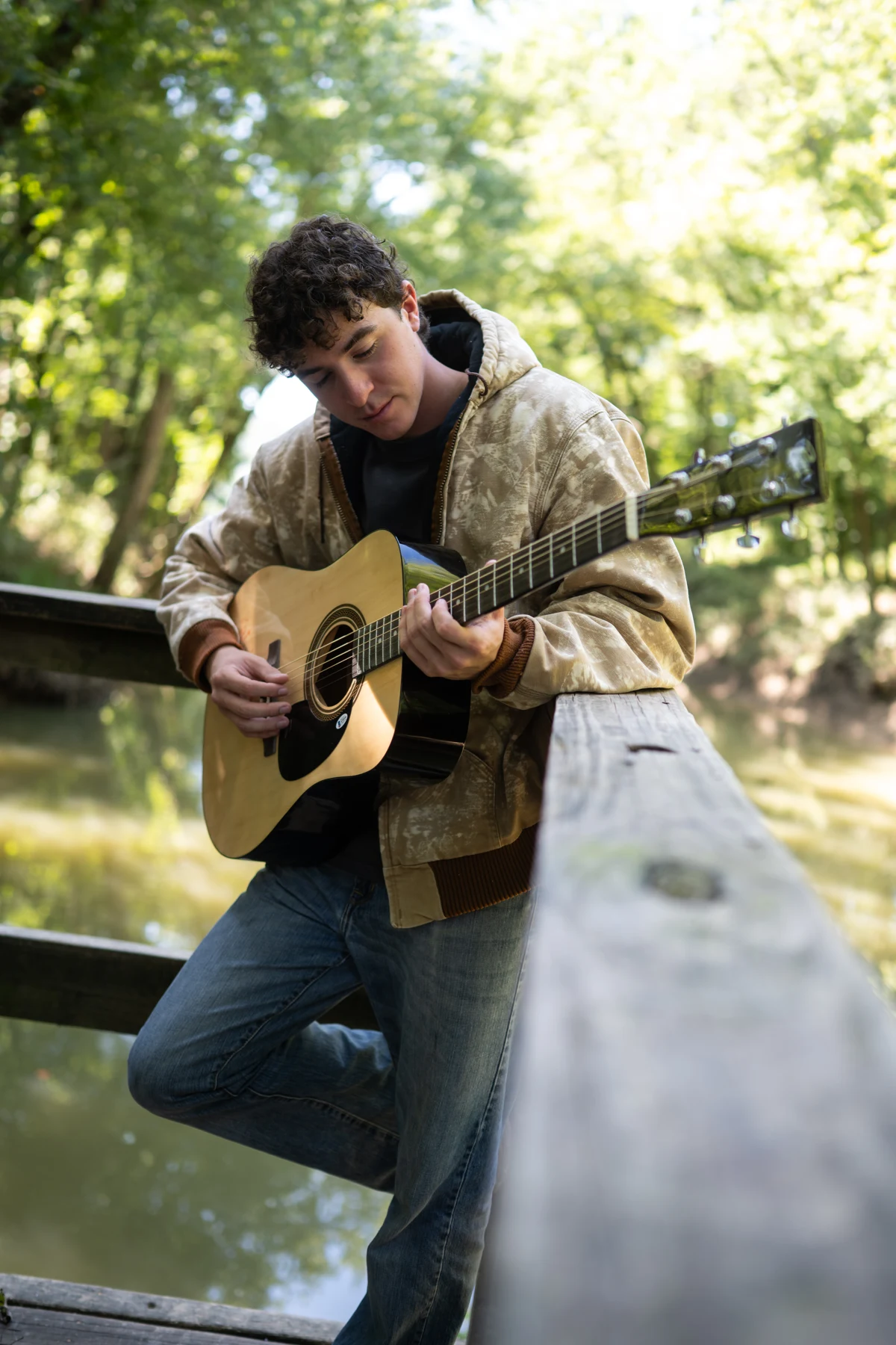 Ryan McKenzie playing acoustic guitar beside a wooded river